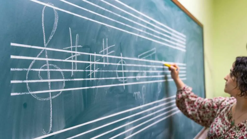 Music teacher writing musical notes on a chalkboard during a music theory lesson in a classroom.