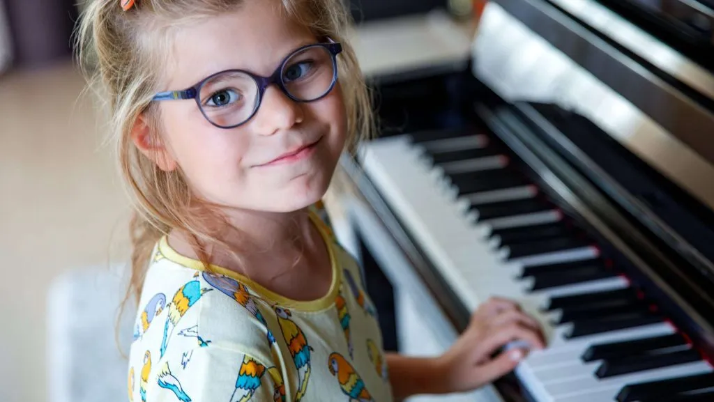 Little school girl learning to play on piano. Cute exciting happy child playng music instrument at home or music school.